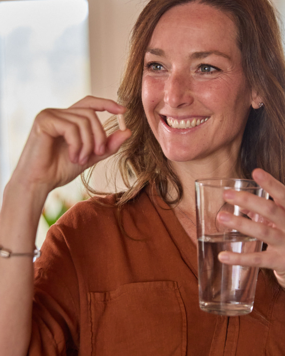 Una mujer sonriente con una cápsula y un vaso de agua