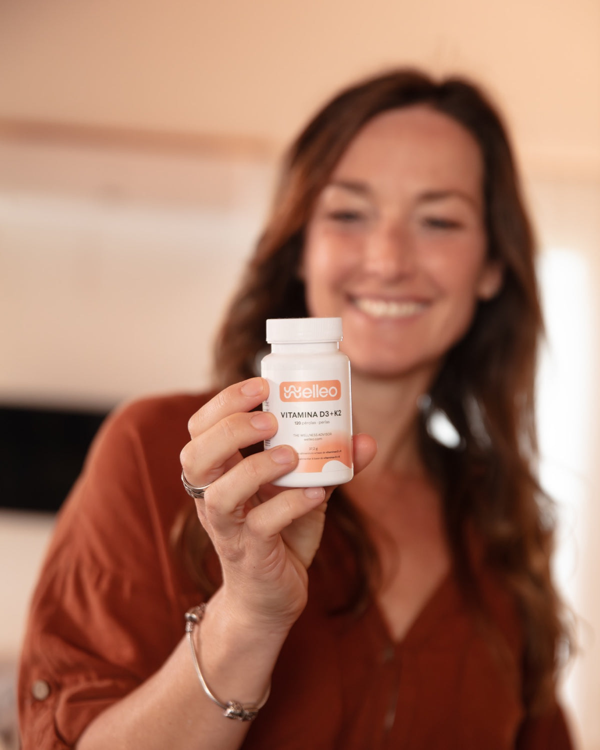 Uma mulher sorridente a segurar um frasco de Vitamina D3+K2 da welleo